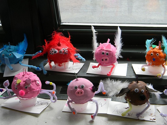 there are many little pigs on display in the window sill, and one pig is wearing feathers