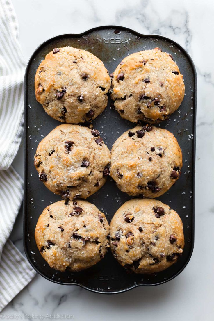 freshly baked chocolate chip muffins on a black tray with a white towel next to it