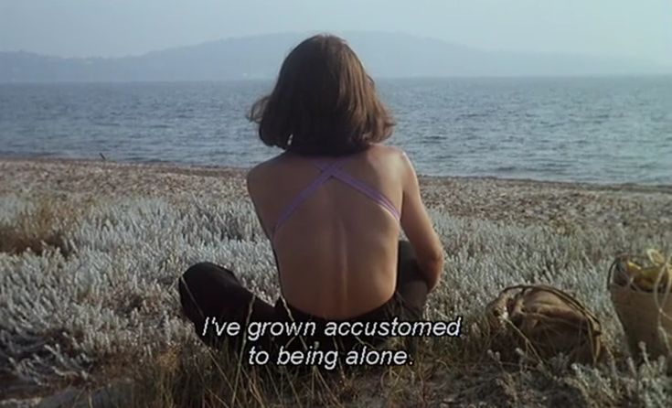 a woman sitting on top of a grass covered field next to the ocean with a quote written in front of her