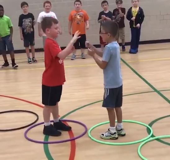 two young boys are playing with hula hoops on the gym floor while others watch