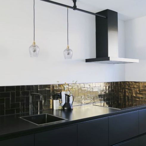 a kitchen with black counter tops and gold backsplash tiles on the back splash