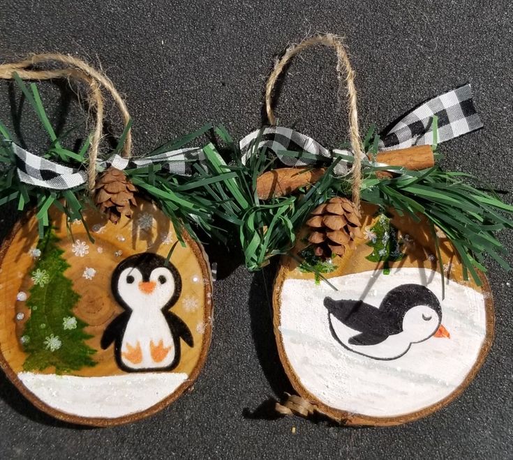 two wooden ornaments with penguins and pine cones on them are hanging from twine strings