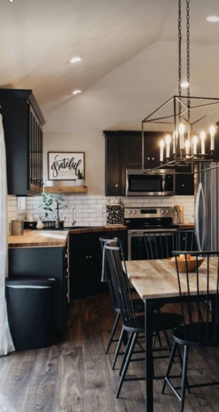 a kitchen and dining room with black cabinets, wood flooring and white brick walls