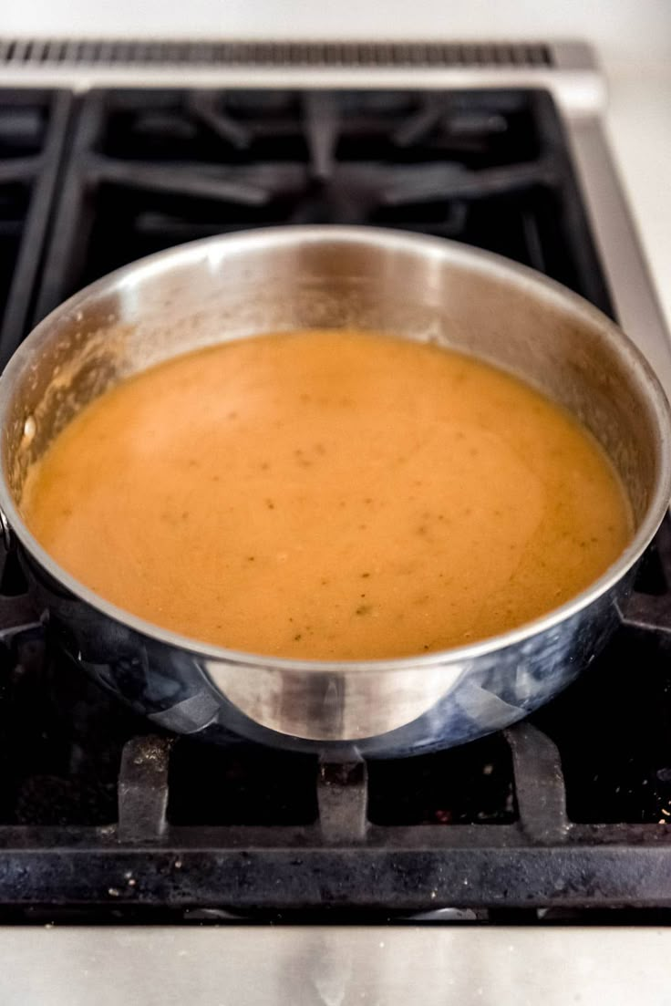 a metal pan filled with soup on top of an open stovetop burner in a kitchen