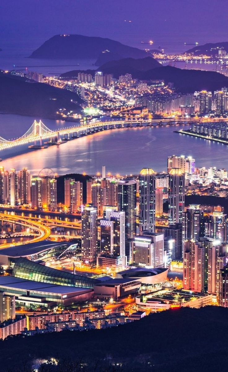 an aerial view of a city at night with lights on the buildings and water in the foreground