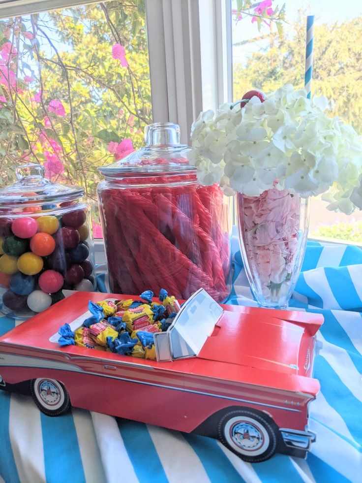 a table with candy and candies in glass jars on it, along with a red toy car