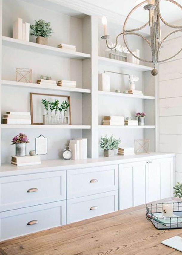 a wooden table sitting in front of a white book shelf filled with books and vases