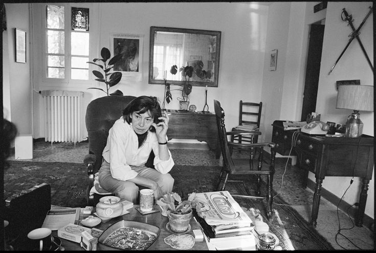 a woman sitting on the floor in her living room talking on a cell phone and eating