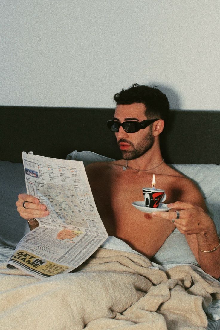 a shirtless man reading a newspaper while holding a coffee cup with a lit candle in it