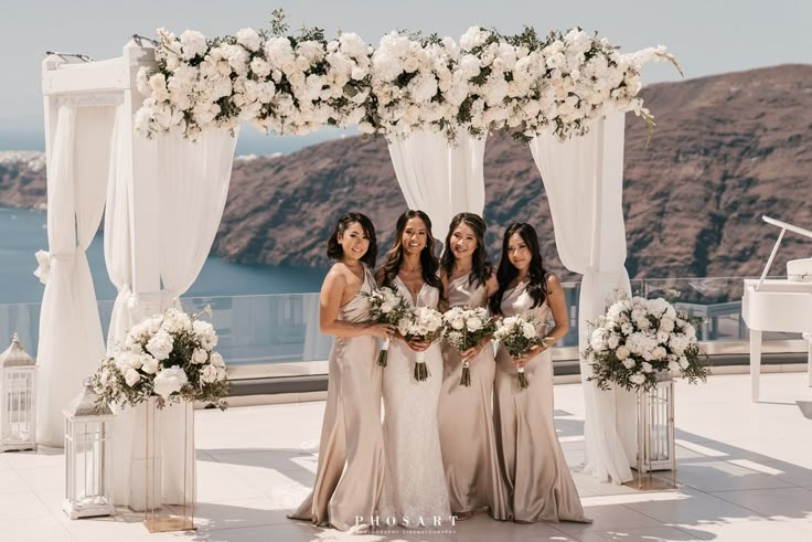 four bridesmaids pose for a photo in front of an arch decorated with white flowers