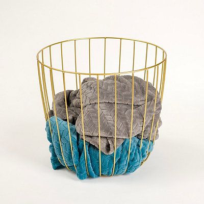 a metal basket filled with blue and grey towels on top of a white floor next to a pile of blankets