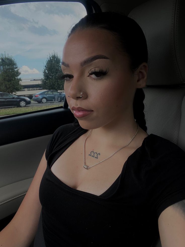 a woman sitting in the back seat of a car wearing a black shirt and silver necklace