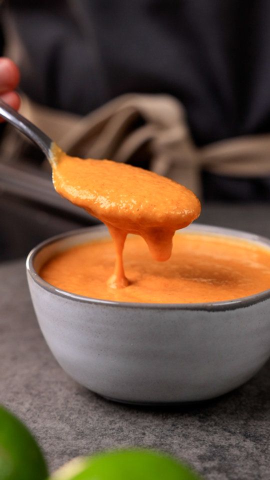 a spoon full of orange sauce being lifted from a bowl with limes in the background