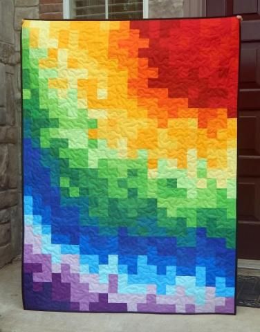 a multicolored quilt hanging on the side of a brick building in front of a door