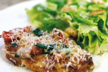 a white plate topped with meat covered in sauce next to a green leafy salad