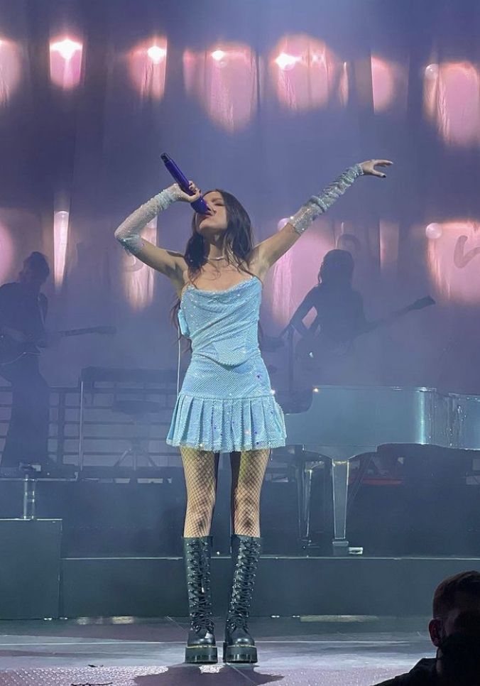 a woman in a short blue dress on stage with her arms up and hands out