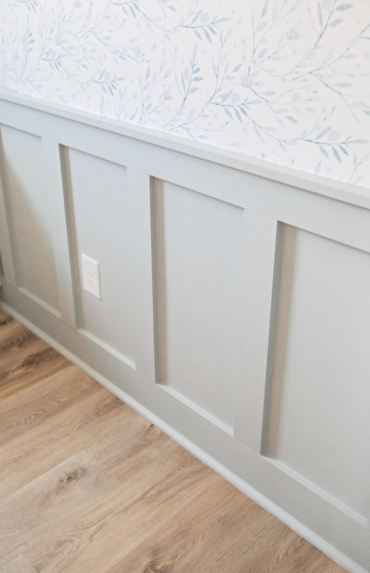 a white bed with wooden floors and wallpaper on the headboard is seen in this image