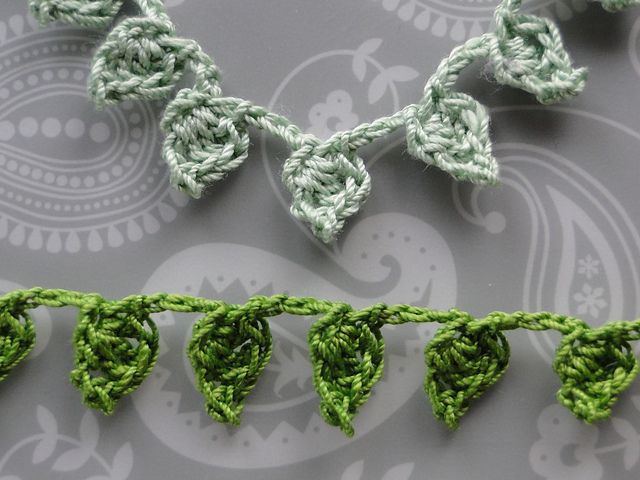 crocheted green leaves are hanging from a string on a gray background with paisley designs