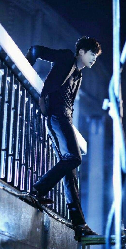 a male in a black shirt and jeans is standing on a ledge with his hand on the railing