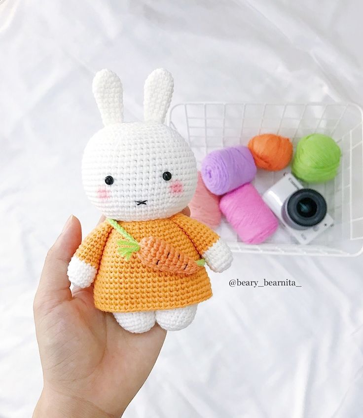 a crocheted bunny doll is held in front of some yarns