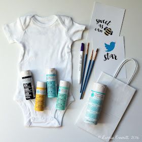 the contents of a baby's bodysuit are laid out next to some paint and brushes