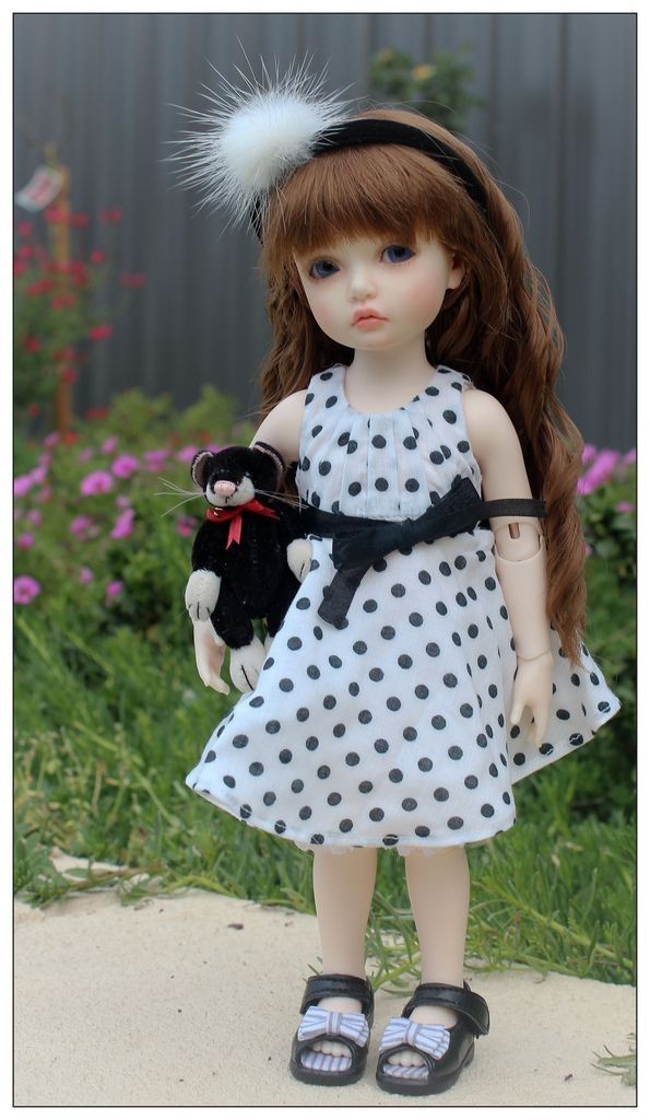 the doll is wearing a dress with polka dots and a black teddy bear in her hand