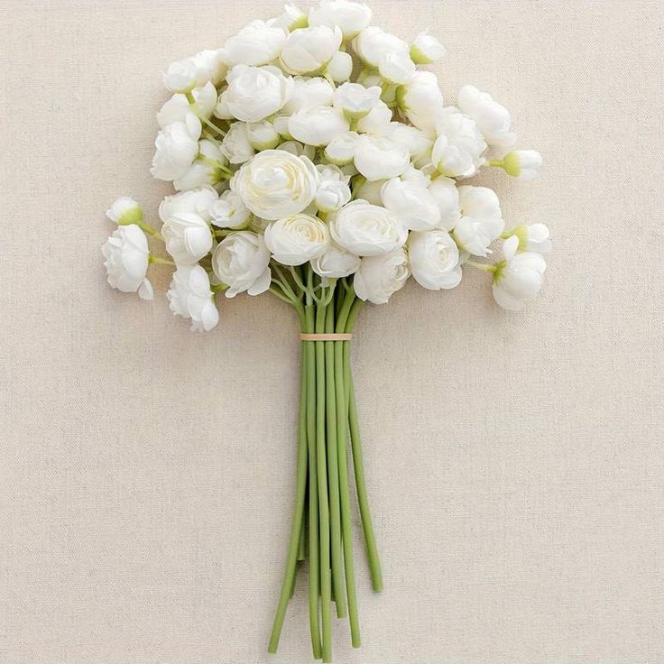 a bouquet of white flowers sitting on top of a beige table next to a wall