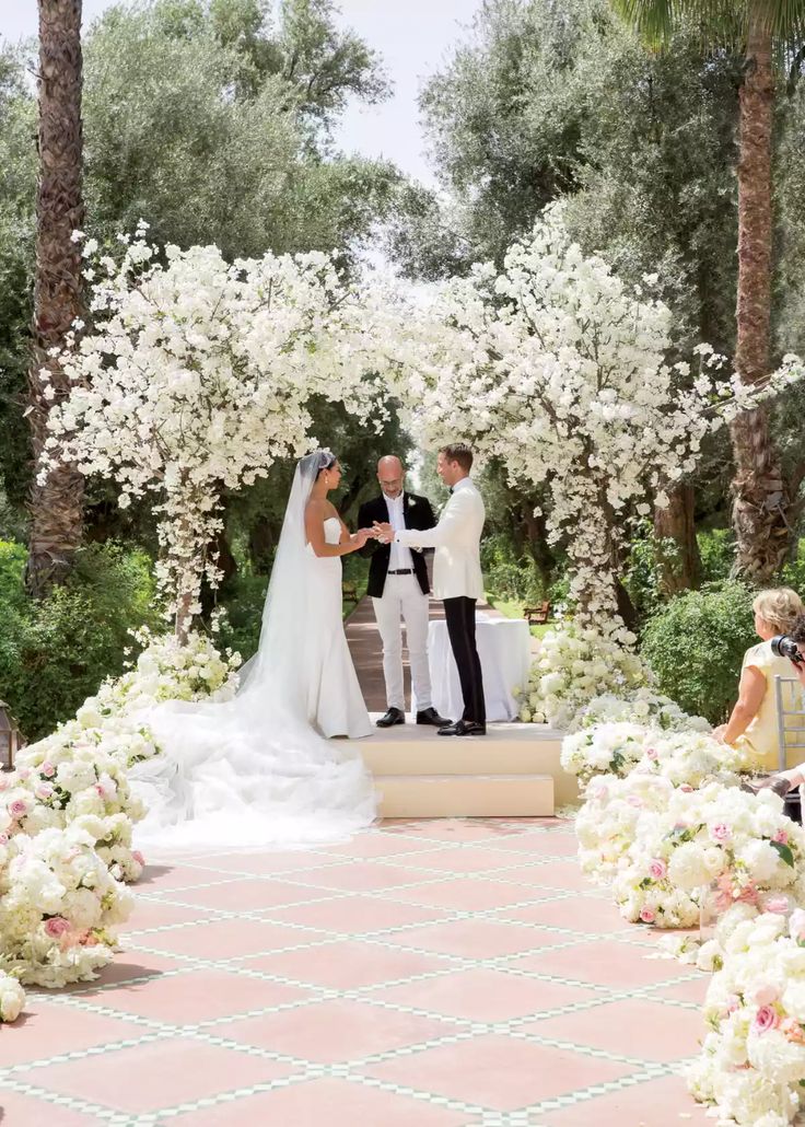 a bride and groom standing at the alter in front of an archway with white flowers