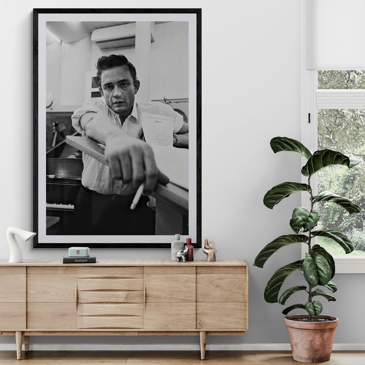 a black and white photo of a man playing the piano in a living room with a potted plant