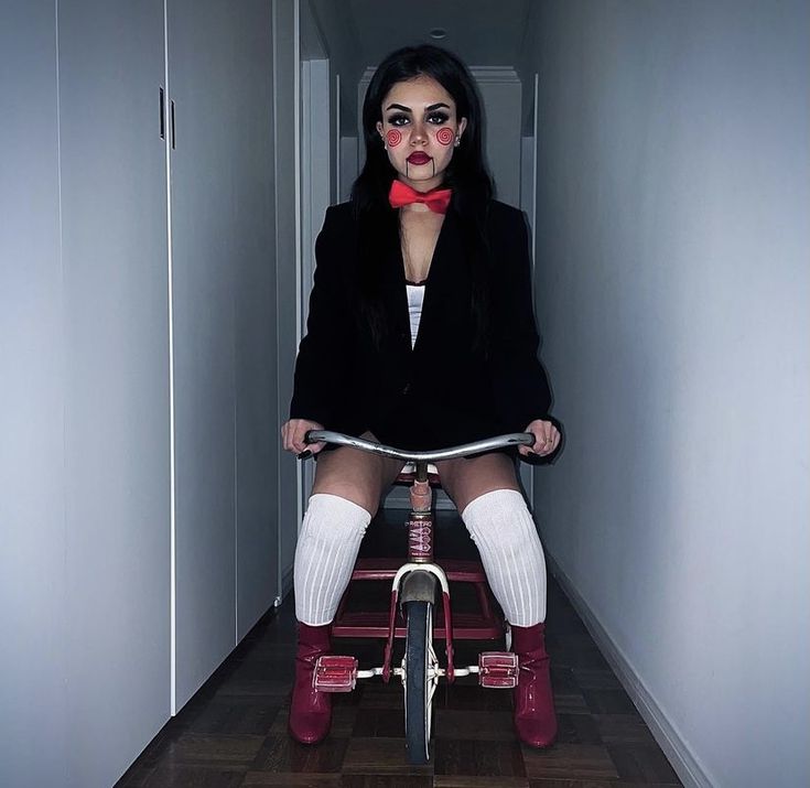 a woman sitting on top of a bike in a hallway with red makeup and stockings