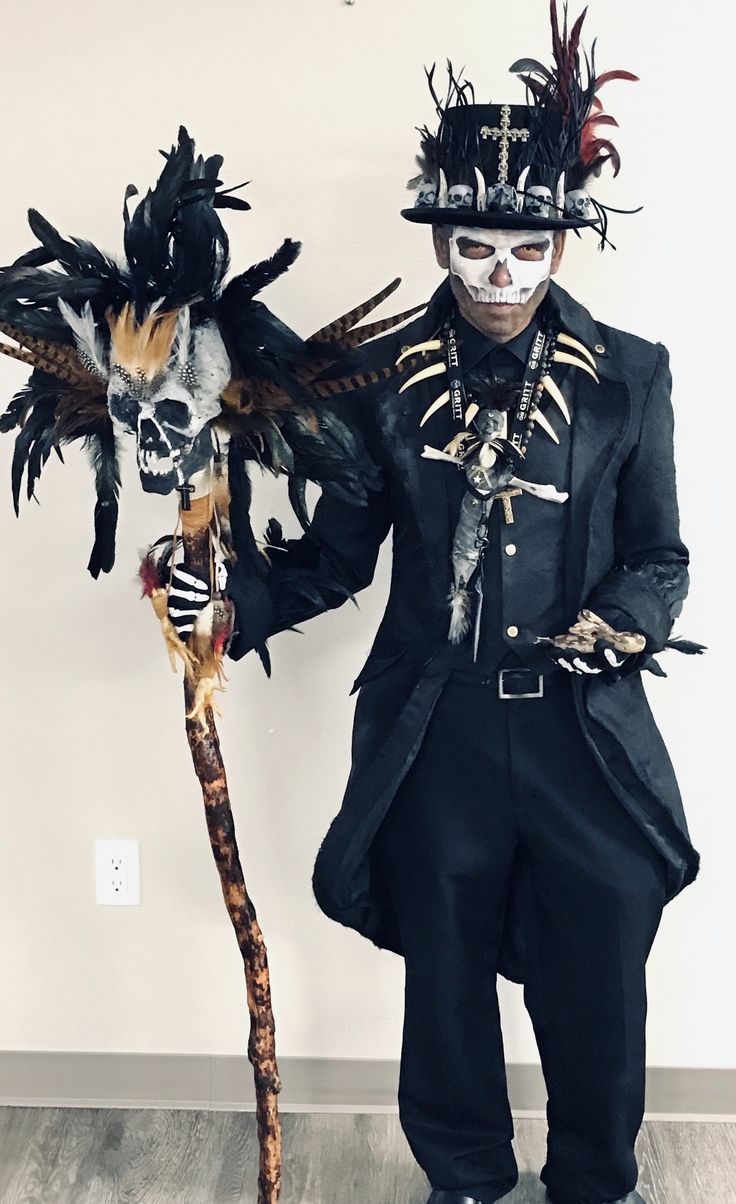 a man dressed up as a skeleton holding a stick and wearing a top hat with feathers on it