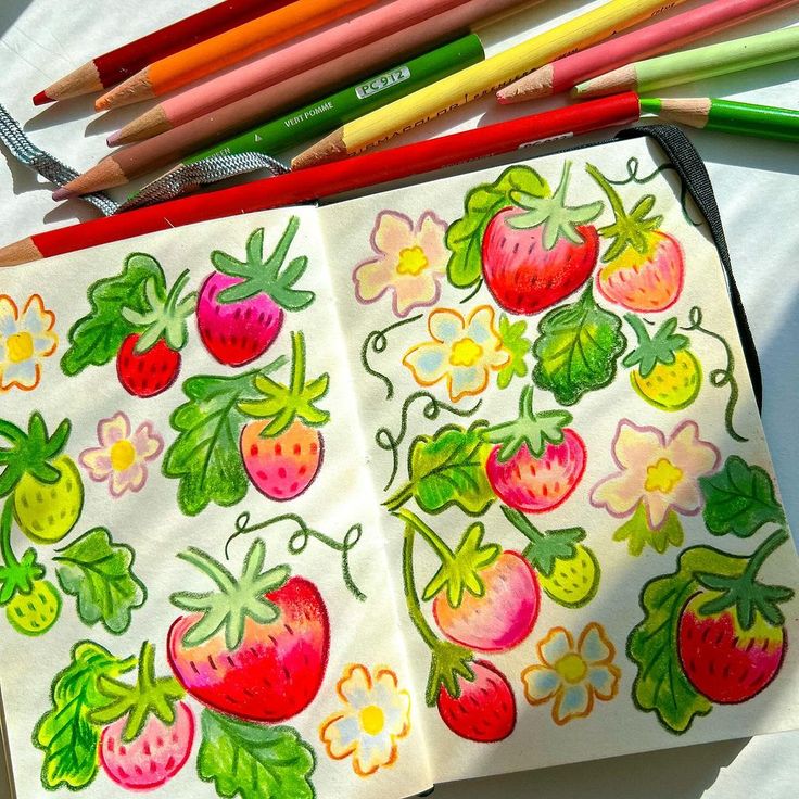 an open notebook with strawberries and flowers drawn on it next to colored pencils