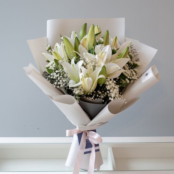 a bouquet of white lilies wrapped in paper on a shelf with a ribbon tied around it