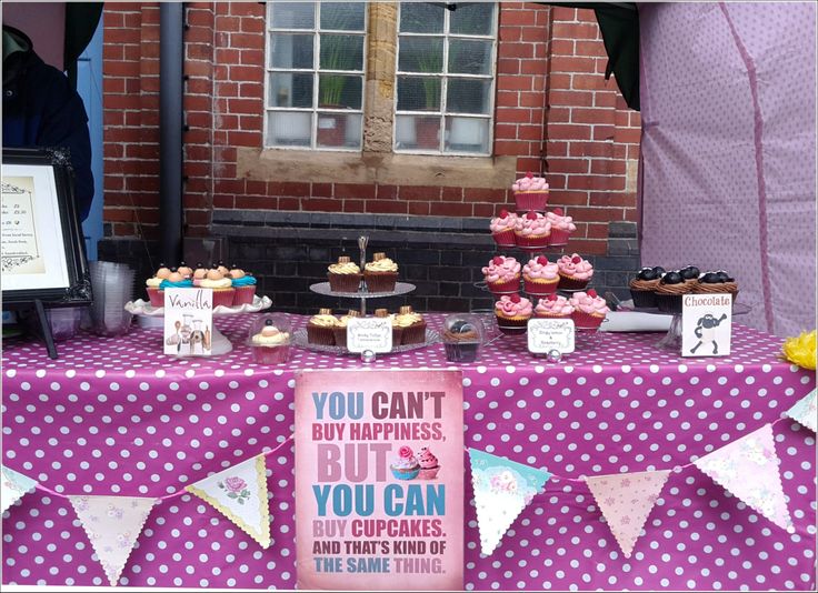 a purple table topped with lots of cupcakes next to a sign that says, you can't buy happiness but you can buy cupcakes