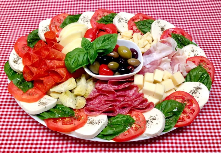 a platter filled with meat, cheese and olives on a red checkered table cloth