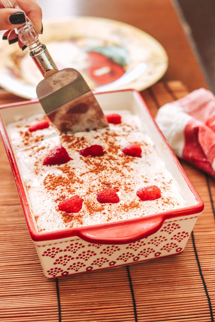 a person is cutting strawberries on top of a cake in a red and white dish