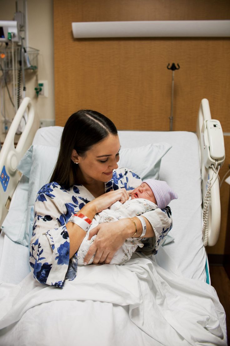 a woman in a hospital bed holding a baby and smiling at the camera with her arm wrapped around him