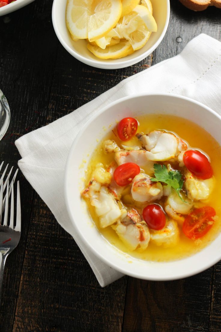 a bowl of soup with shrimp, tomatoes and lemons on the side next to silverware