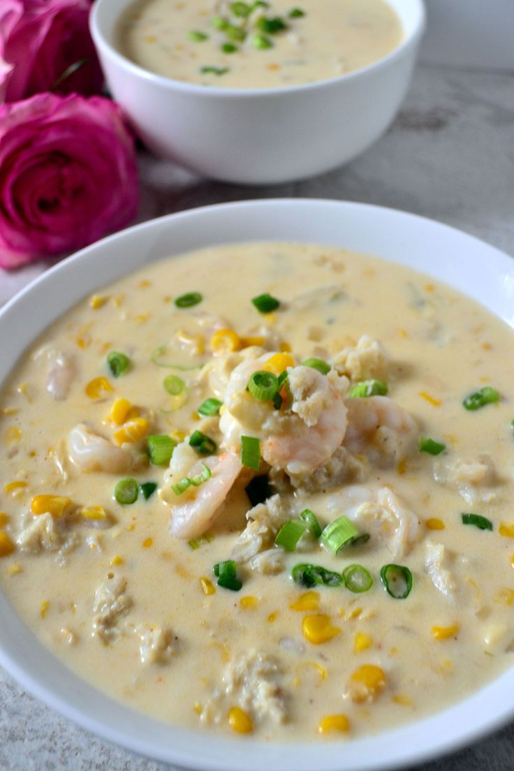 two bowls of soup with shrimp, corn and green onions next to pink roses on a table