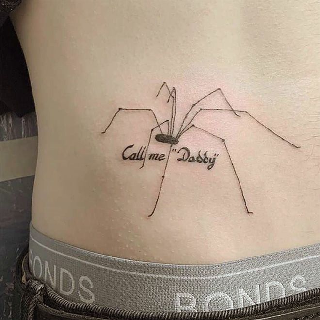 a woman's lower back tattoo with the words call me daddy and a spider on it