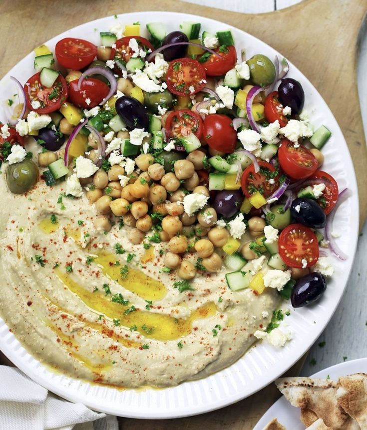 a white plate topped with hummus, olives and tomatoes