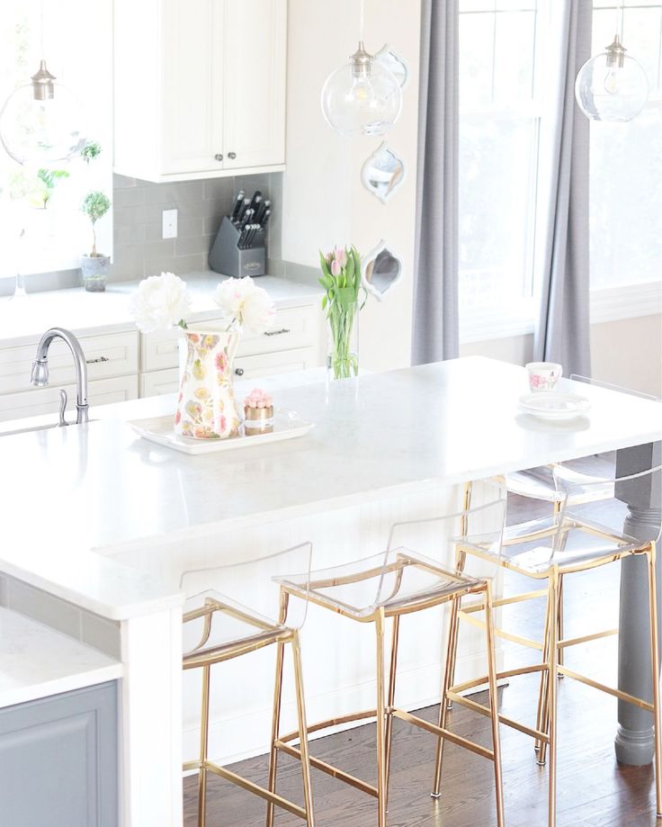 a white kitchen with gold bar stools and marble counter tops in the center island