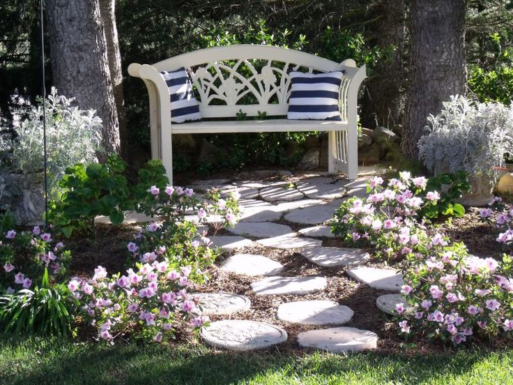 a white bench sitting in the middle of a garden with purple flowers and rocks around it