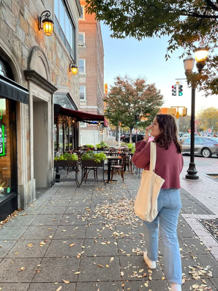 a woman is walking down the sidewalk with her hand in her pocket and looking at something