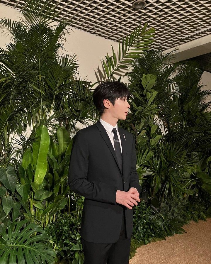 a man in a suit and tie standing next to plants