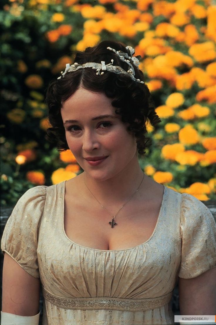 a woman in an old fashioned dress is smiling at the camera with flowers behind her