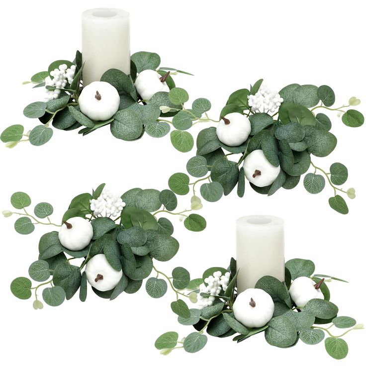 two white candles are surrounded by green leaves and flowers on each candle holder in the shape of an apple