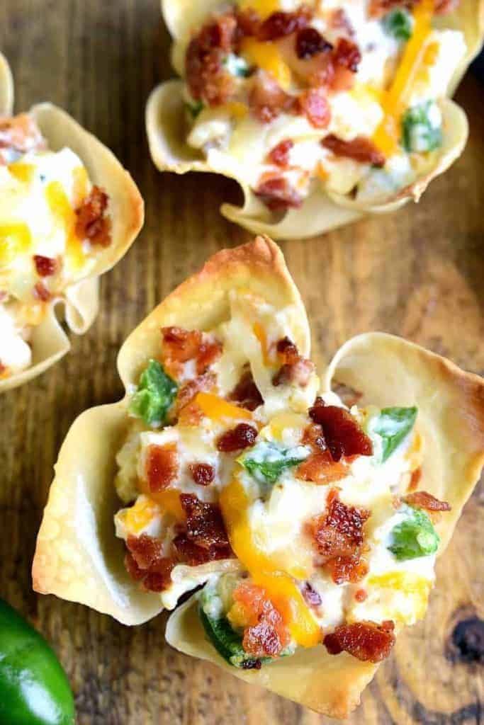 mini pizza cups filled with bacon, cheese and green peppers on a wooden table next to a lime