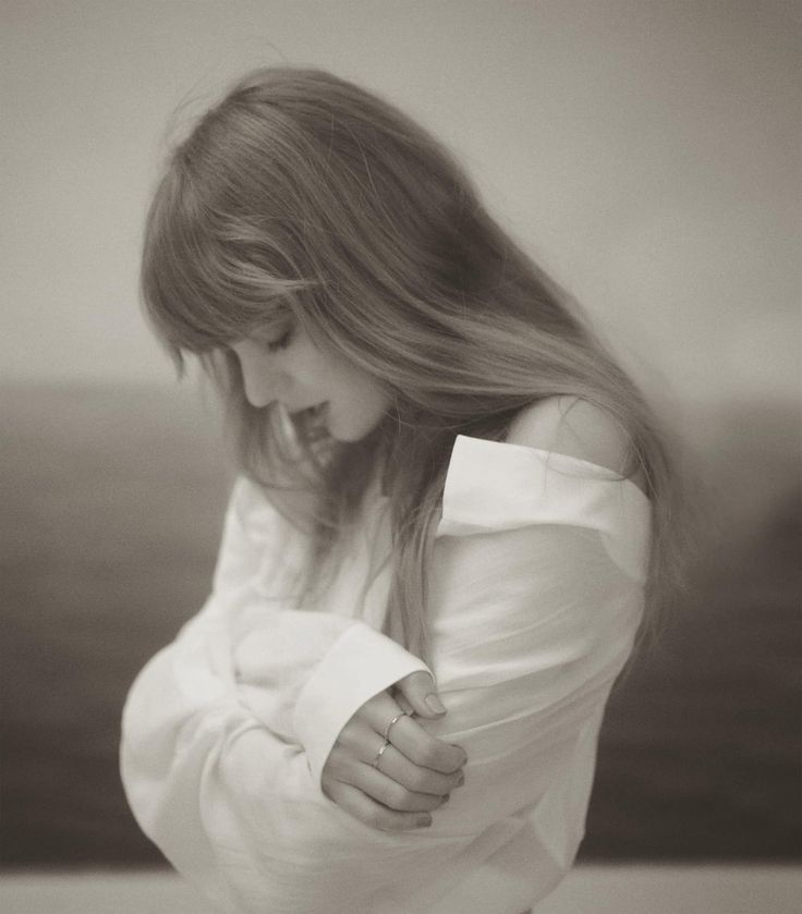 a woman with long hair is standing in front of the ocean wearing a white shirt