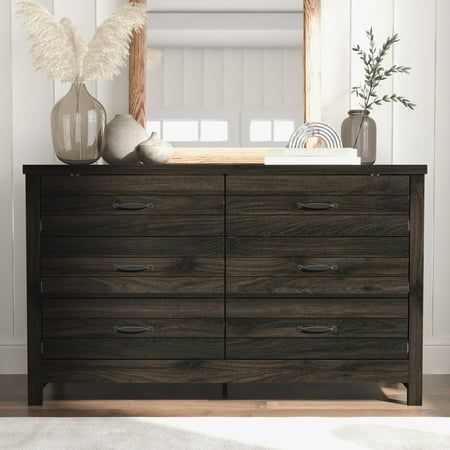 a dresser with a mirror and vases on top of it in front of a white wall